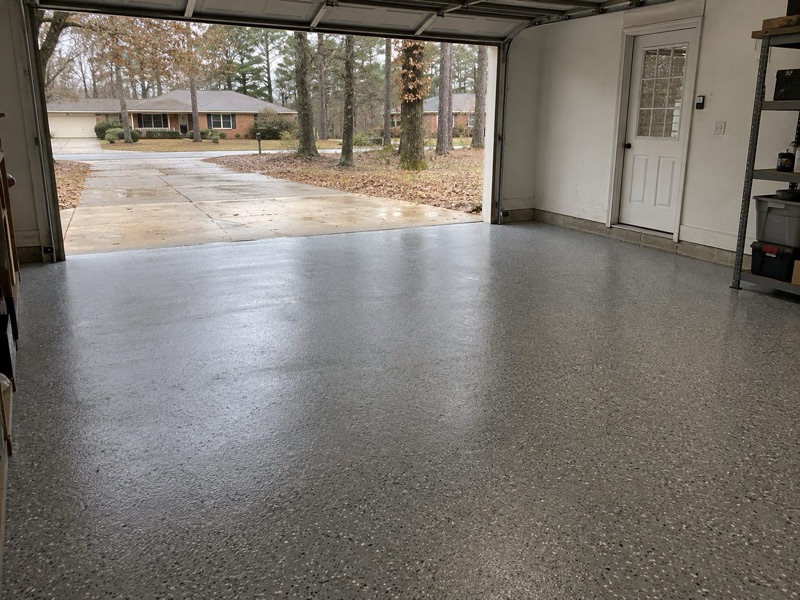 Speckled gray flake floor in a garage with the door open to a wet driveway